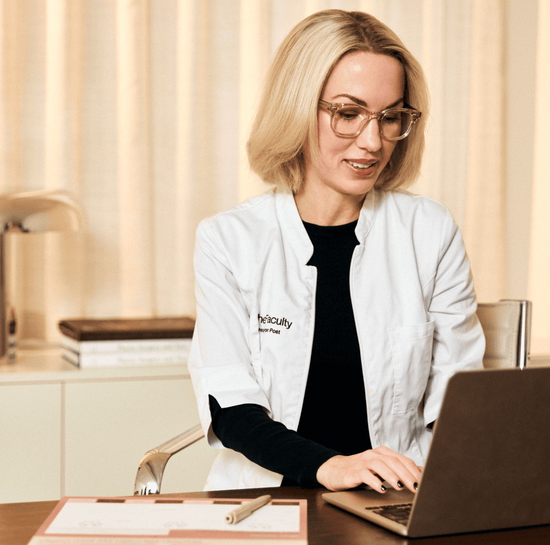 Kvinna i vit labbrock arbetar på laptop i kontorsmiljö.
