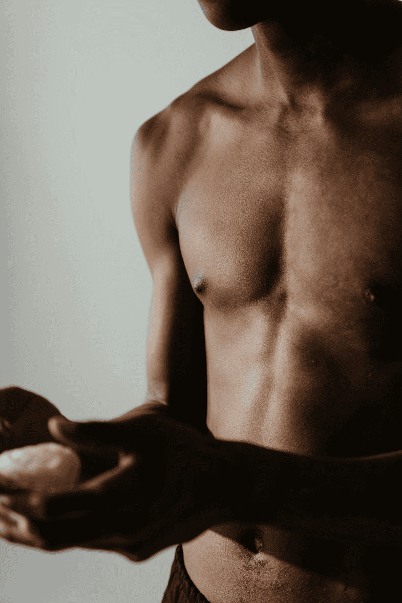 Mans torso with defined muscles holding a small object in hands.